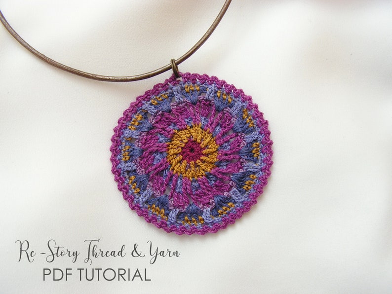 May include: A crocheted pendant necklace with a purple, blue, and gold mandala design. The necklace is made with a brown metal chain.