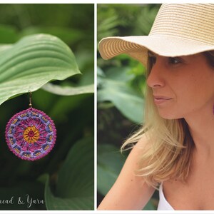May include: A pair of crocheted earrings with a mandala design in shades of purple, pink, and yellow. The earrings are hanging from a leaf.