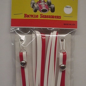May include: A package of red and white bicycle streamers with silver bells and hooks. The package has a yellow and red label that says "Speedway Bicycle Streamers" with a cartoon race car and the text "Made in USA".