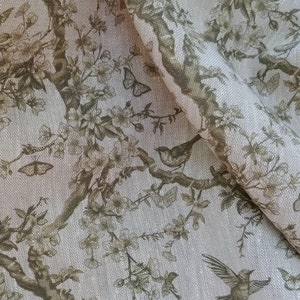Pode incluir: Um tecido bege com um padrão repetitivo de pássaros e borboletas estilizados marrons em um galho com pequenas flores brancas.