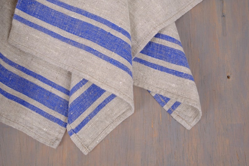 May include: A folded linen kitchen towel with blue stripes on a wooden surface.