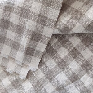 May include: A close-up of a folded piece of fabric with a white and gray gingham pattern. The fabric is woven with a textured, linen-like appearance.