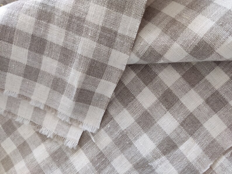 May include: A close-up of a folded piece of fabric with a white and gray gingham pattern. The fabric is woven with a textured, linen-like appearance.