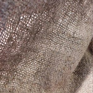 May include: Close-up of a brown burlap fabric with a woven texture. The fabric is folded and shows the intricate details of the weave.