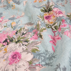 May include: A close-up of a light blue fabric with a floral pattern. The flowers are pink, yellow, and white, and the leaves are green. The fabric has a textured surface.