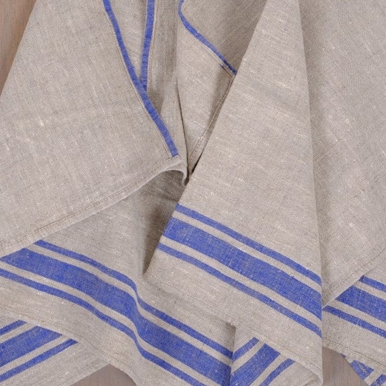 May include: A folded linen tea towel with blue stripes. The towel is made of natural linen and has a rustic look.