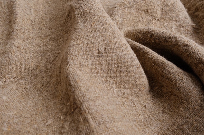 May include: Close-up of a textured, brown burlap fabric with a rough, woven texture. The fabric is folded and wrinkled, creating a natural, rustic look.