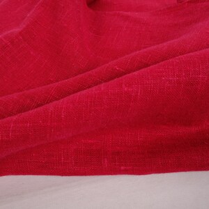 May include: A close-up of a deep red fabric with a textured weave. The fabric is folded and draped, showing its soft, drapey texture.