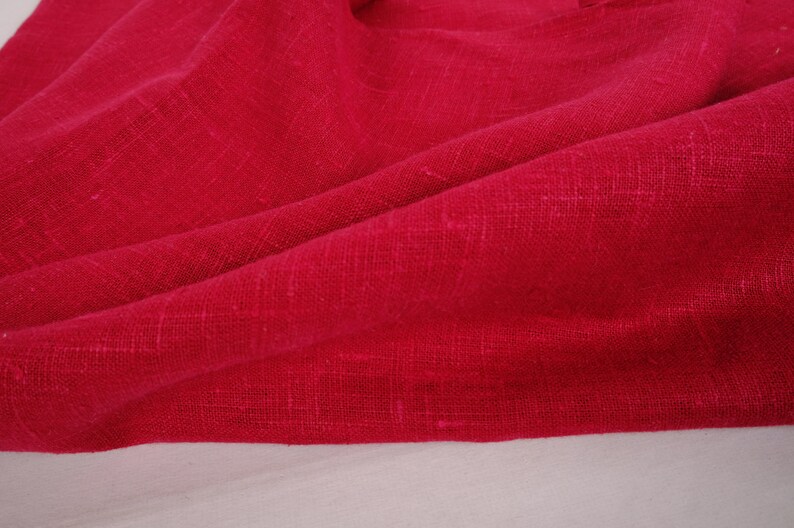 May include: A close-up of a deep red fabric with a textured weave. The fabric is folded and draped, showing its soft, drapey texture.