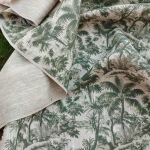 May include: A folded piece of fabric with a tropical forest print. The design features palm trees and other foliage in shades of green and gray against a light beige background. The fabric appears to be linen or a similar natural material.