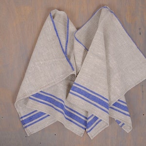 May include: A folded linen tea towel with blue stripes. The towel is made of natural linen and has a rustic look.