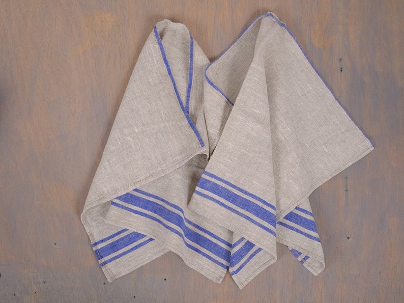 May include: A folded linen tea towel with blue stripes. The towel is made of natural linen and has a rustic look.