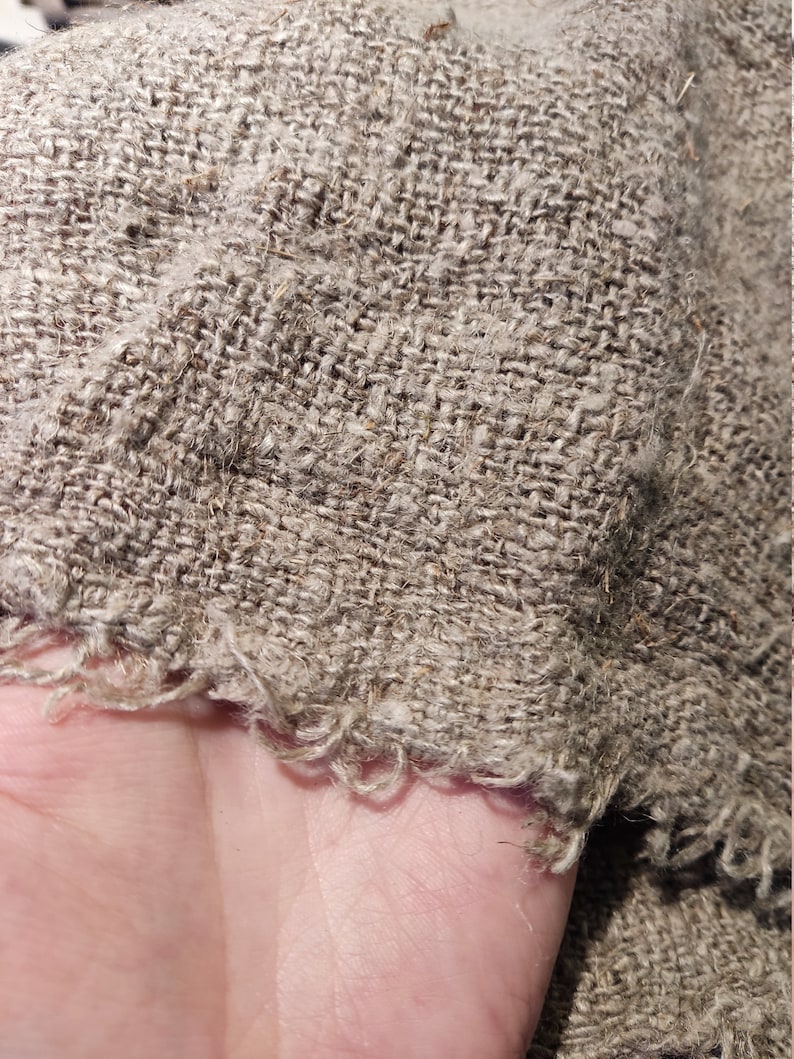 May include: Close-up of a piece of natural linen fabric with a rough, textured surface. The fabric has a frayed edge.