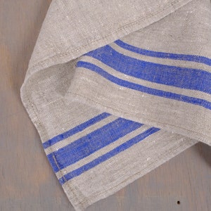 May include: A folded linen kitchen towel with blue stripes. The towel is made of natural linen fabric and has a rustic look.