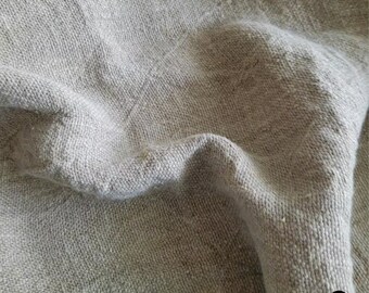 Op de afbeelding: Close-up van een natuurlijke linnen stof met een textuur geweven. De stof is licht beige van kleur en heeft een licht gerimpeld uiterlijk.