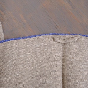 May include: A close-up of a natural linen fabric with a blue trim. The fabric is folded in half and the blue trim is visible on both sides.