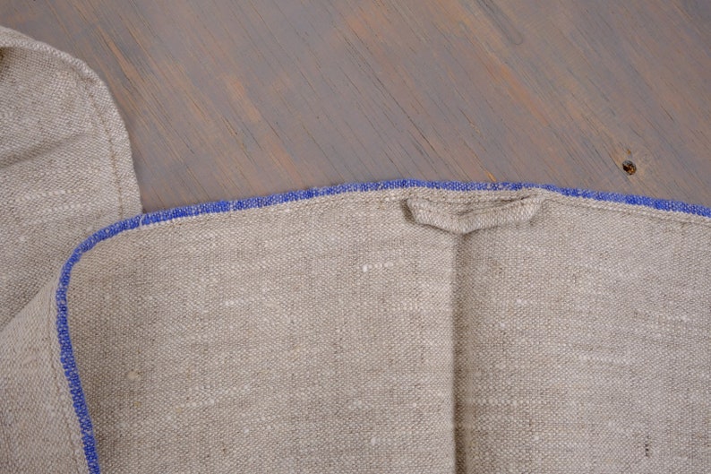May include: A close-up of a natural linen fabric with a blue trim. The fabric is folded in half and the blue trim is visible on both sides.