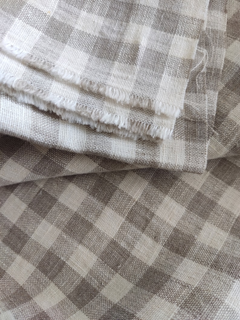 May include: A close-up of a folded piece of fabric with a brown and white gingham pattern. The fabric is soft and textured, with a slightly frayed edge.