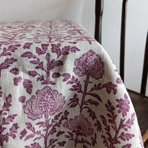 Puede incluir: Una tela de lino blanca con un patrón repetido de diseños florales morados. La tela tiene una textura sutil y una sensación suave y natural.