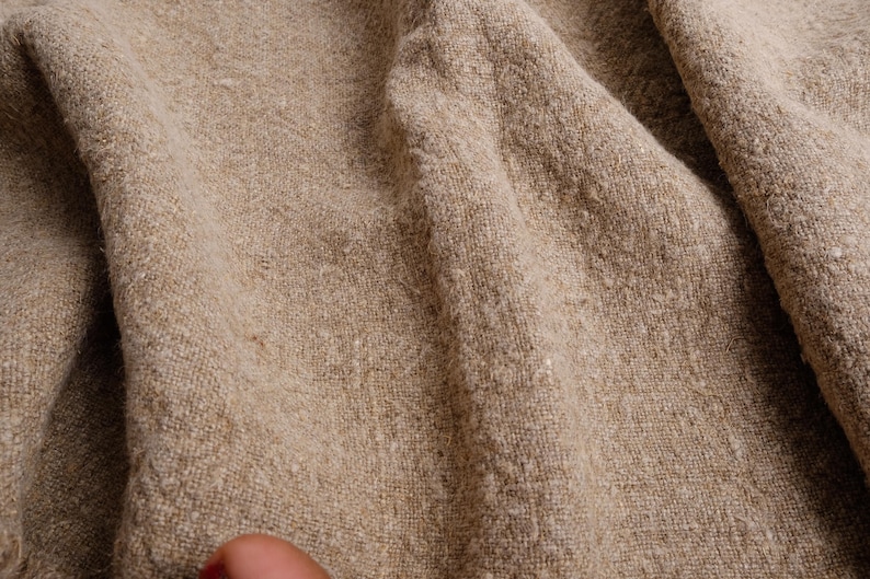 May include: Close-up of a natural linen fabric with a textured, woven pattern. The fabric is folded and has a light brown color.