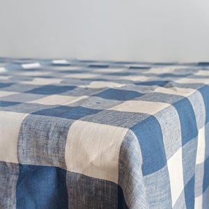 Puede incluir: Un mantel a cuadros azules y blancos con textura de lino. El mantel está doblado por la mitad y tiene un aspecto suave y casual.