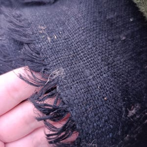 Può includere: Primo piano di un tessuto blu scuro intrecciato con un bordo sfilacciato. Il tessuto ha una trama ruvida e fibre visibili, con alcuni fili sciolti e piccole particelle sparse sulla superficie. Il bordo è strappato e irregolare.
