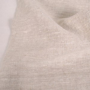 May include: Close-up of a natural linen fabric with a textured weave. The fabric is a light beige color and has a slightly wrinkled appearance.