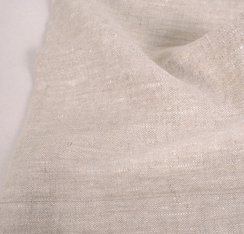 May include: Close-up of a natural linen fabric with a textured weave. The fabric is a light beige color and has a slightly wrinkled appearance.