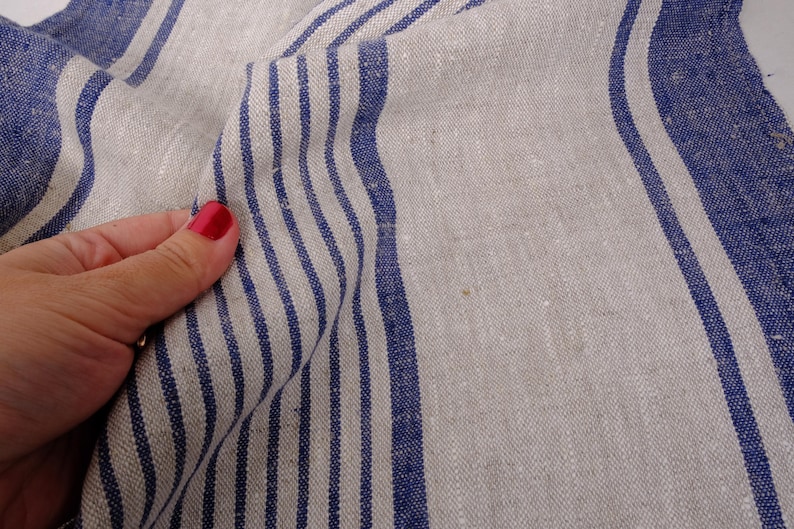 May include: Close-up of a white linen fabric with blue stripes. The fabric is folded and has a natural, textured look.