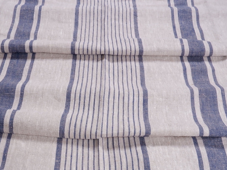 May include: A close-up of a linen fabric with blue and white stripes. The fabric is folded in thirds, showing the pattern.