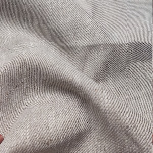 May include: Close-up of a light brown linen fabric with a subtle herringbone weave. The fabric is soft and textured, with a natural, rustic look.