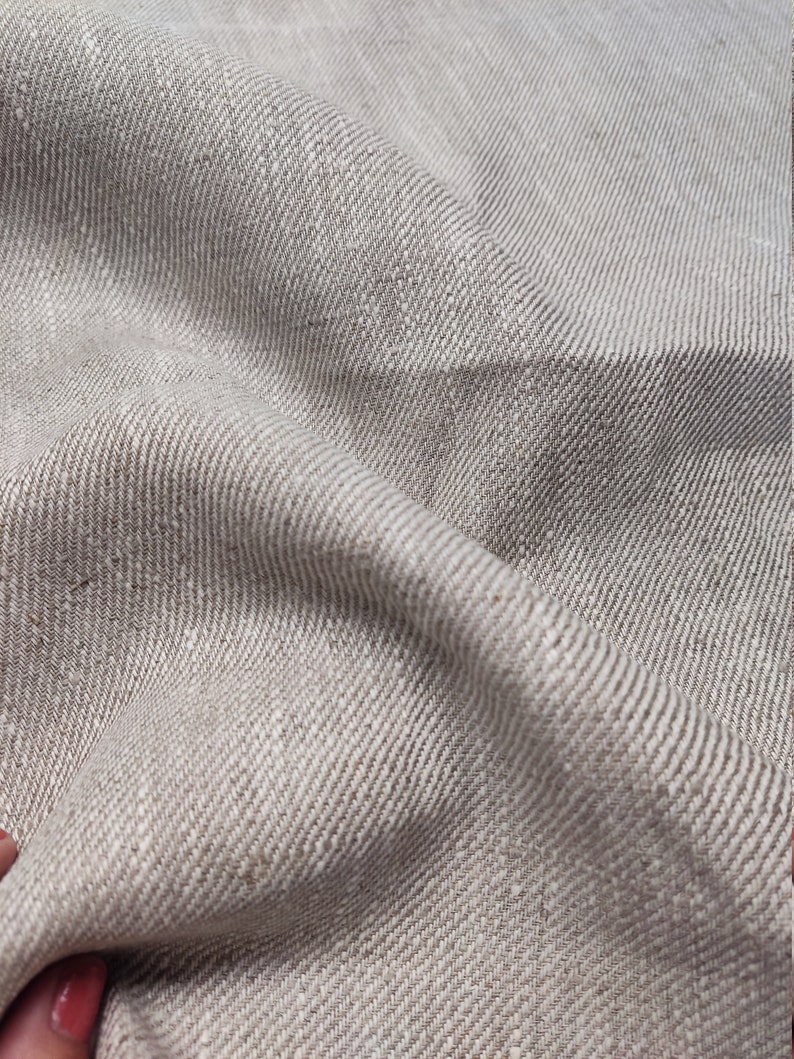 May include: Close-up of a light brown linen fabric with a subtle herringbone weave. The fabric is soft and textured, with a natural, rustic look.