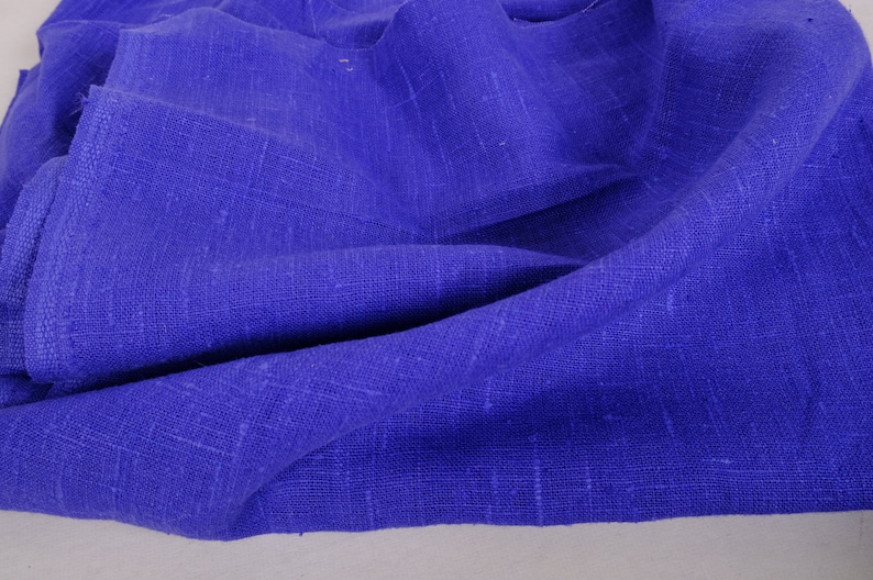 May include: A close-up of a blue fabric with a textured weave. The fabric is folded and draped, showing its soft and drapey texture.