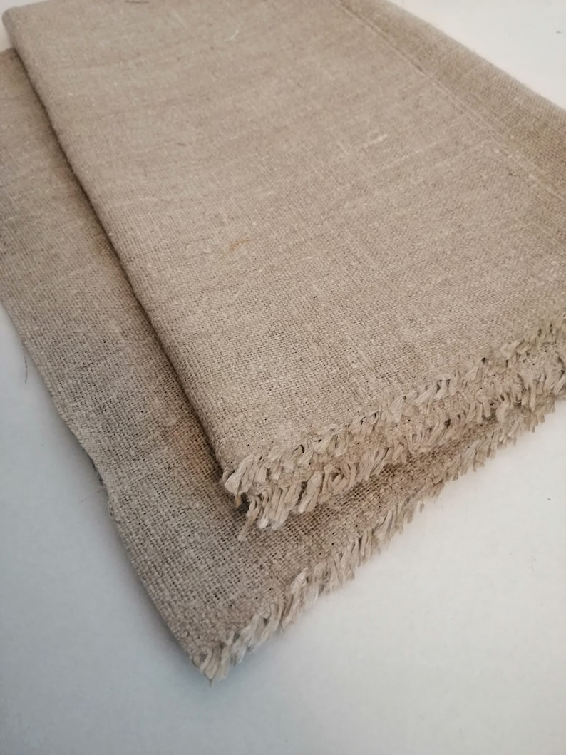 Puede incluir: Dos piezas de tela de lino natural con bordes deshilachados. La tela es de color beige claro y tiene una textura tejida.