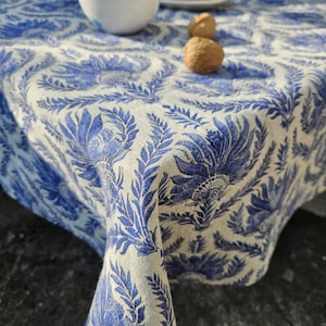 May include: A white tablecloth with a blue floral pattern. The tablecloth is made of linen and has a slightly textured surface.