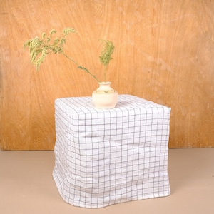 Puede incluir: Un jarrón de cerámica blanco con un patrón marrón y blanco se encuentra sobre un mantel a cuadros blanco y negro. El jarrón contiene un ramo de flores silvestres amarillas secas.