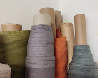 Könnte beinhalten: Eine Sammlung von Stoffrollen in verschiedenen Farben, darunter Grau, Grün, Orange und Blau, die in Pappröhren verpackt sind. Die Stoffrollen sind auf einer weißen Oberfläche gestapelt.