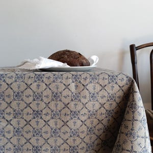 May include: A brown loaf of bread on a white plate, sitting on a beige tablecloth with a blue floral pattern.