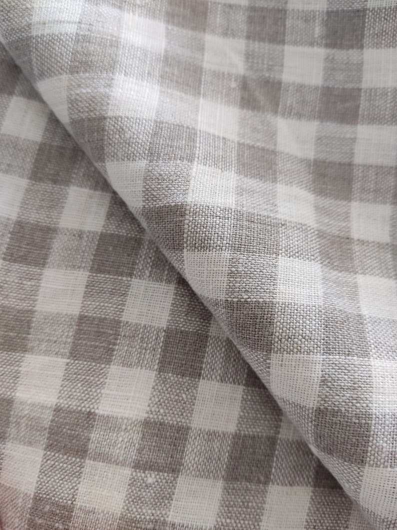May include: A close-up of a white and gray gingham fabric. The fabric has a woven texture and is folded in half.