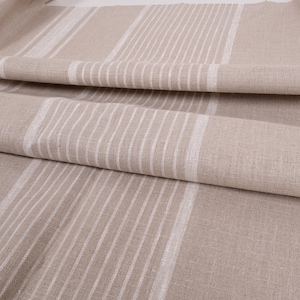 May include: Close-up of a beige linen fabric with white stripes. The fabric is folded and has a textured surface.