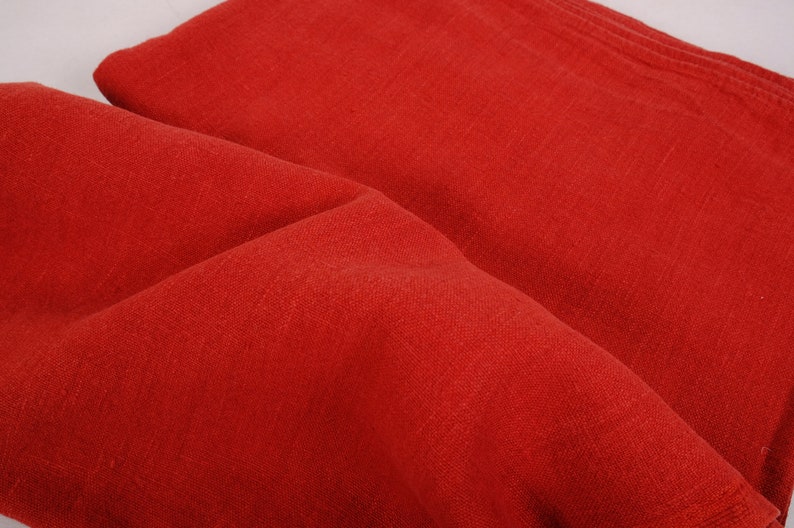 May include: A close-up of a red fabric with a textured surface. The fabric is folded in half and the folds create a soft, rounded shape.