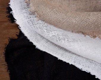 May include: Three layers of fabric with raw, frayed edges stacked on top of each other. The top layer is a natural tan burlap, the middle layer is a white open-weave mesh fabric, and the bottom layer is a solid black woven textile material.