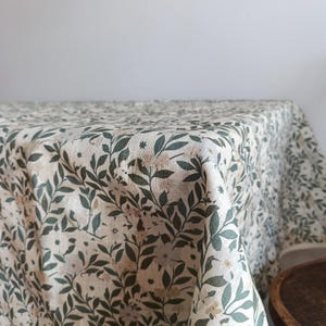 May include: A white tablecloth with a green leafy pattern. The tablecloth is made of linen and has a subtle texture.