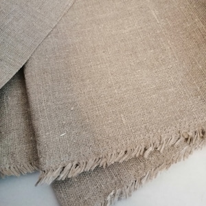 Puede incluir: Dos piezas de tela de lino natural con bordes deshilachados. La tela es de color beige claro y tiene una textura tejida.