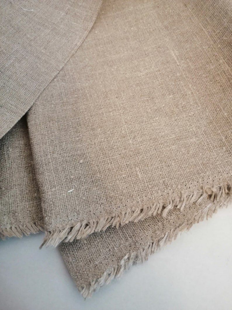 Puede incluir: Dos piezas de tela de lino natural con bordes deshilachados. La tela es de color beige claro y tiene una textura tejida.