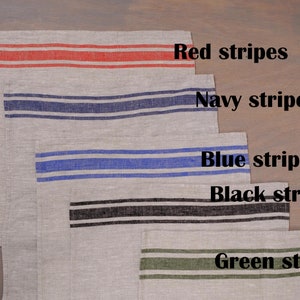 May include: Five linen tea towels with different colored stripes. The towels are arranged in a stack, with the red striped towel on top and the green striped towel on the bottom. The towels are labeled with the color of their stripes: red, navy, blue, black, and green.