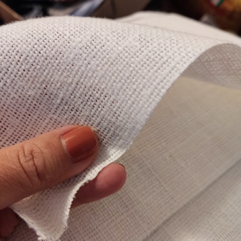 Puede incluir: Primer plano de una tela blanca con textura tejida. La tela est&aacute; doblada y sostenida por un dedo con esmalte de u&ntilde;as marr&oacute;n claro.