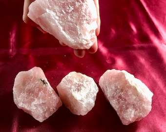 May include: Three pink rose quartz crystals of varying sizes and shapes on a red satin background.