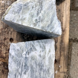 Puede incluir: Tres piezas rectangulares de piedra verde pálido y blanco, cortadas en bruto, con vetas visibles. La piedra tiene un aspecto natural y texturizado. Las piezas están dispuestas sobre una superficie de madera envejecida, lo que sugiere una materia prima o un suministro artesanal.