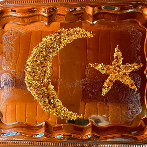 Könnte beinhalten: Ein silbernes Serviertablett mit einem Halbmond- und Sternendesign aus goldenem Glitzer.